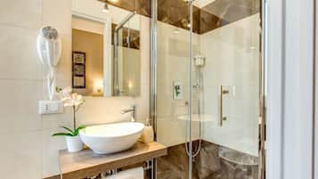 Un bagno moderno con un ampio lavandino bianco, box doccia in vetro e zona doccia rivestita in marmo.