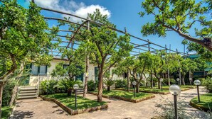 A courtyard with stone pathways, green lawns, and trees. - Hotel Florida (Sorrento)