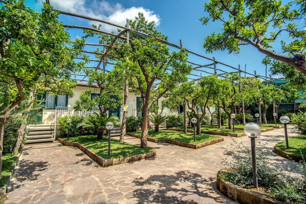 A courtyard with stone pathways, green lawns, and trees. - Hotel Florida (Sorrento)