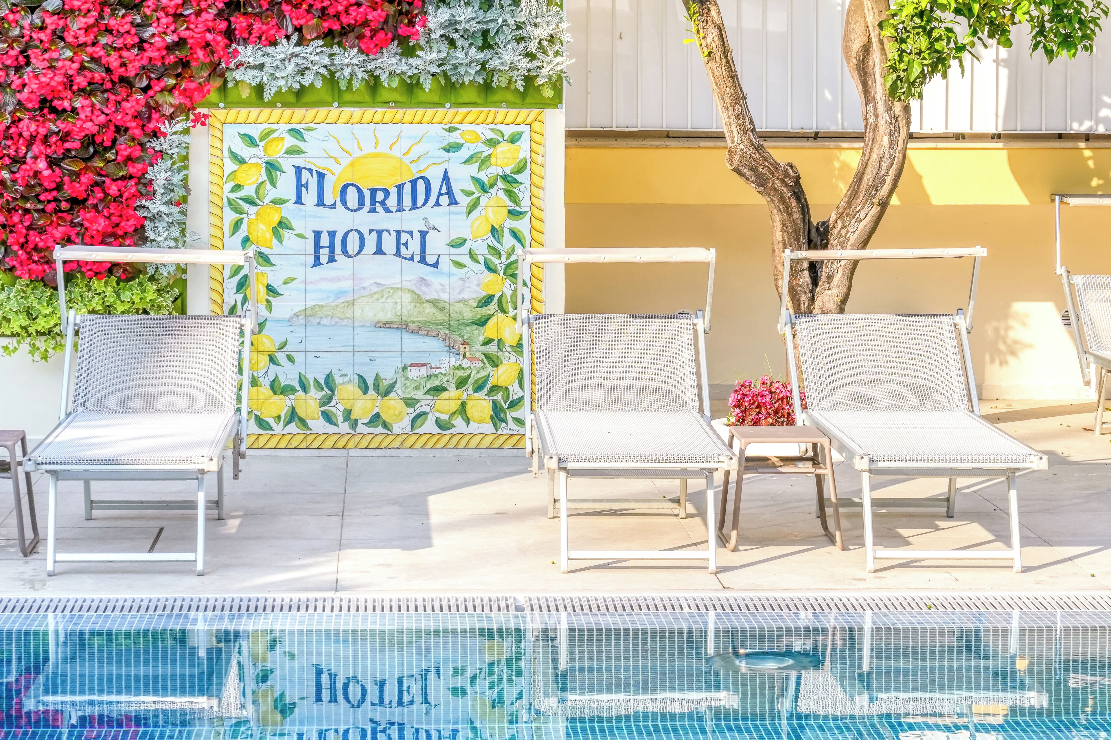 A pool area with lounge chairs, a sign reading 'Florida Hotel,' and a tiled wall with a sun and lemon design.