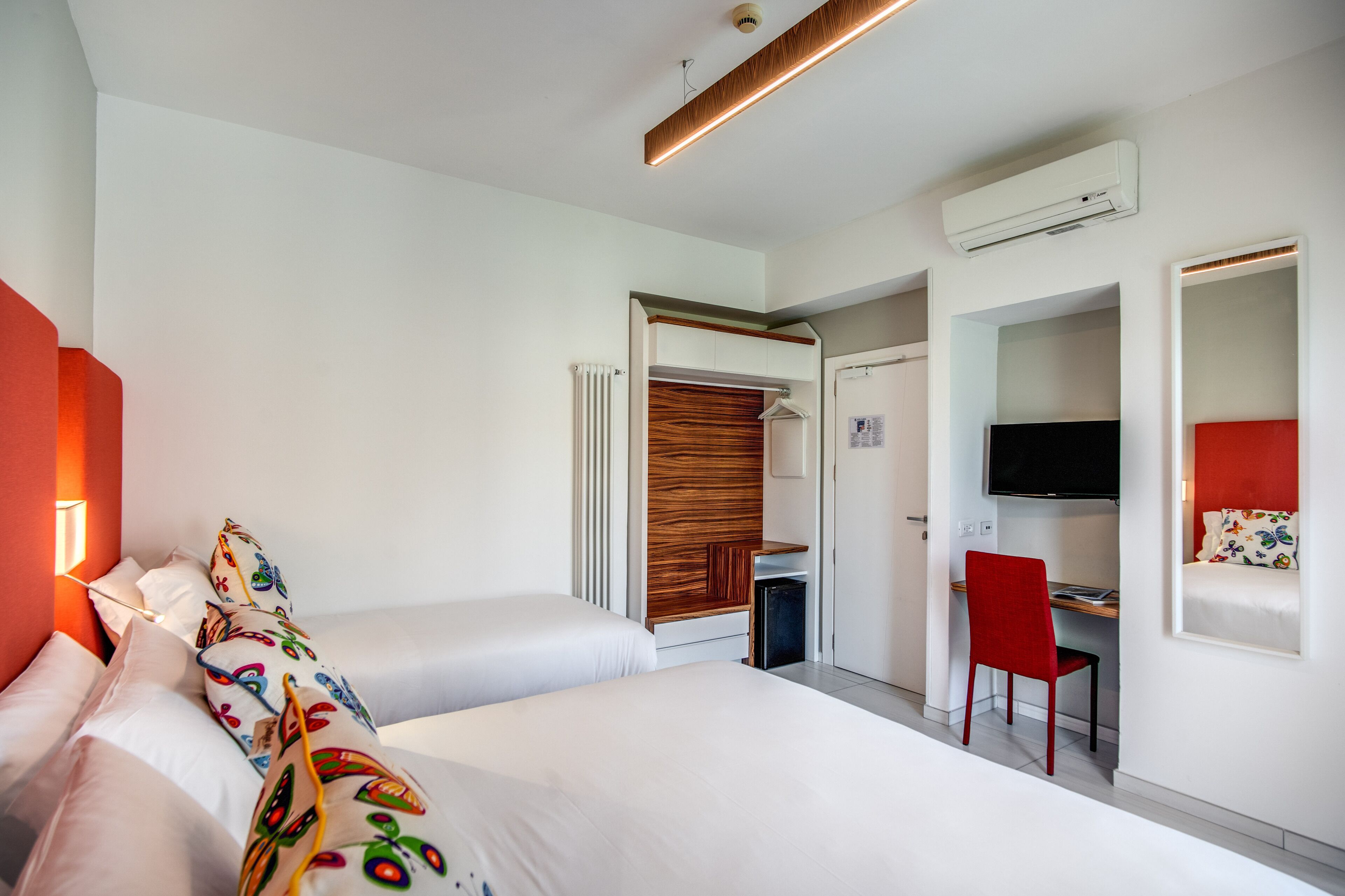 A modern hotel room with two beds, a desk, a TV, and a wardrobe.