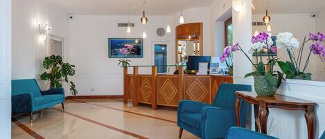 A lobby with teal chairs, a reception desk, a large mirror, and a TV screen.