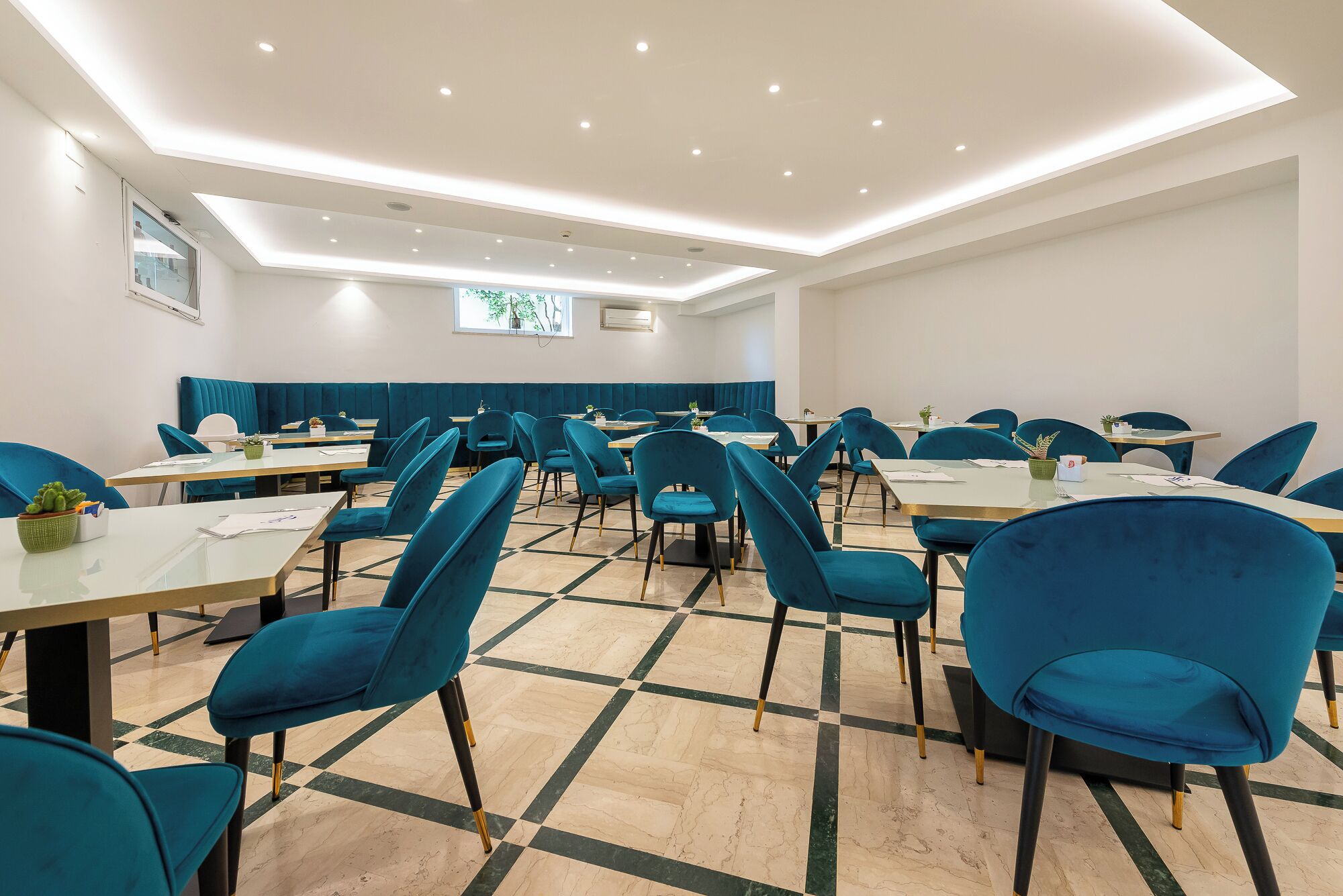 Un salón de conferencias con sillas color turquesa, mesas blancas y un piso con diseño de cuadros.