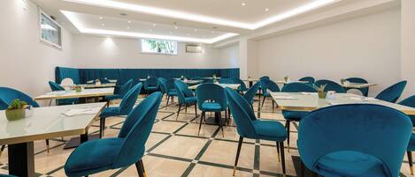 Un salón de conferencias con sillas color turquesa, mesas blancas y un piso con diseño de cuadros.