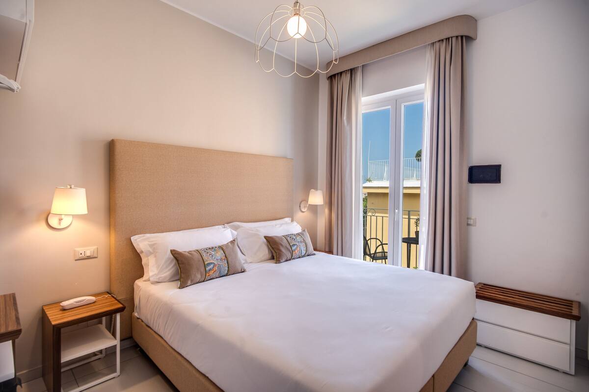A neatly made bed with a headboard, two bedside lamps, and a nightstand with a phone.