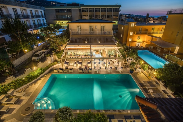Un espace piscine aménagé sur le toit, avec un bar à l’intérieur d’une structure en verre, des chaises longues et un escalier en colimaçon menant à l’étage supérieur.