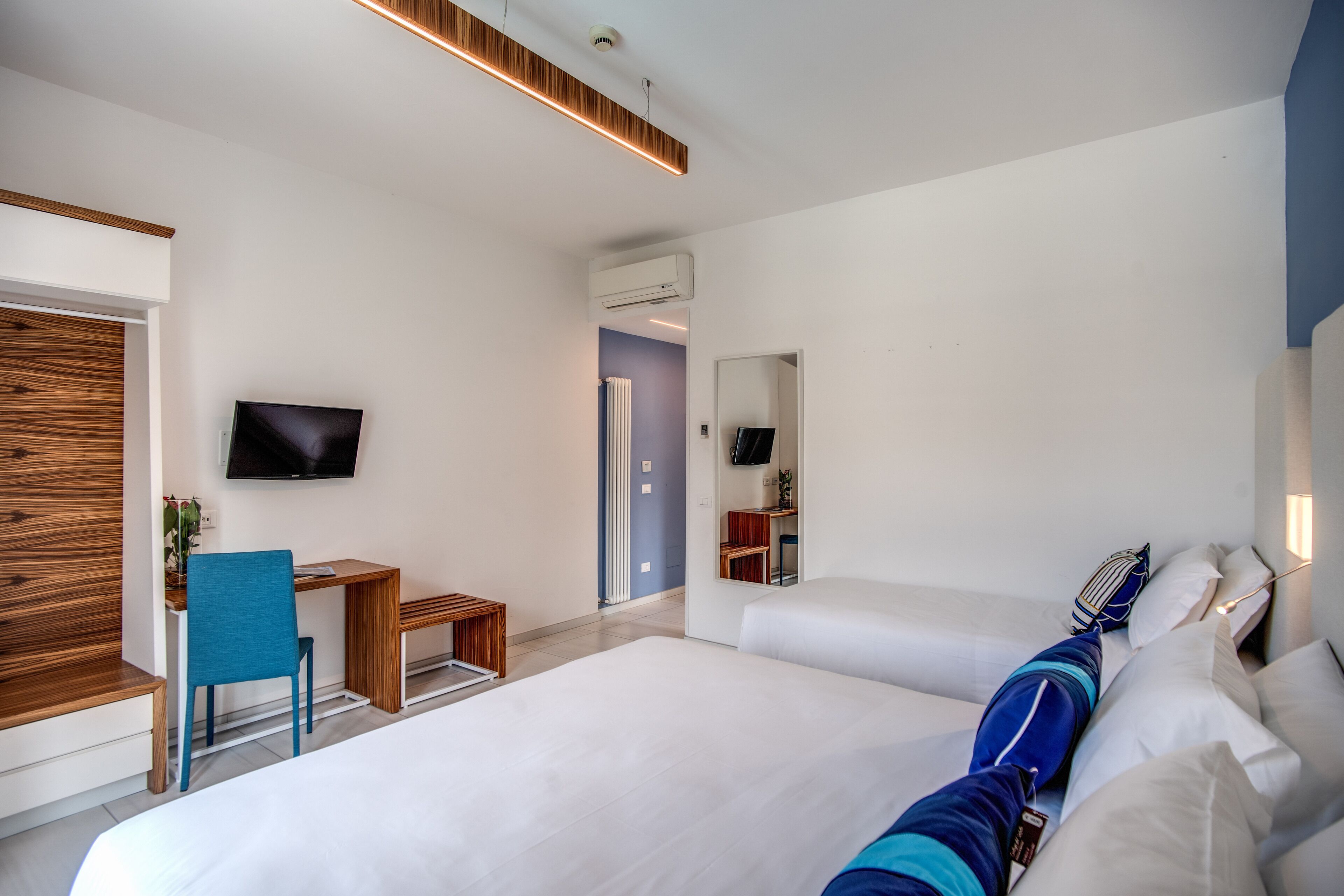 A modern hotel room with a large bed, a desk, a chair, a television, and a mirror.