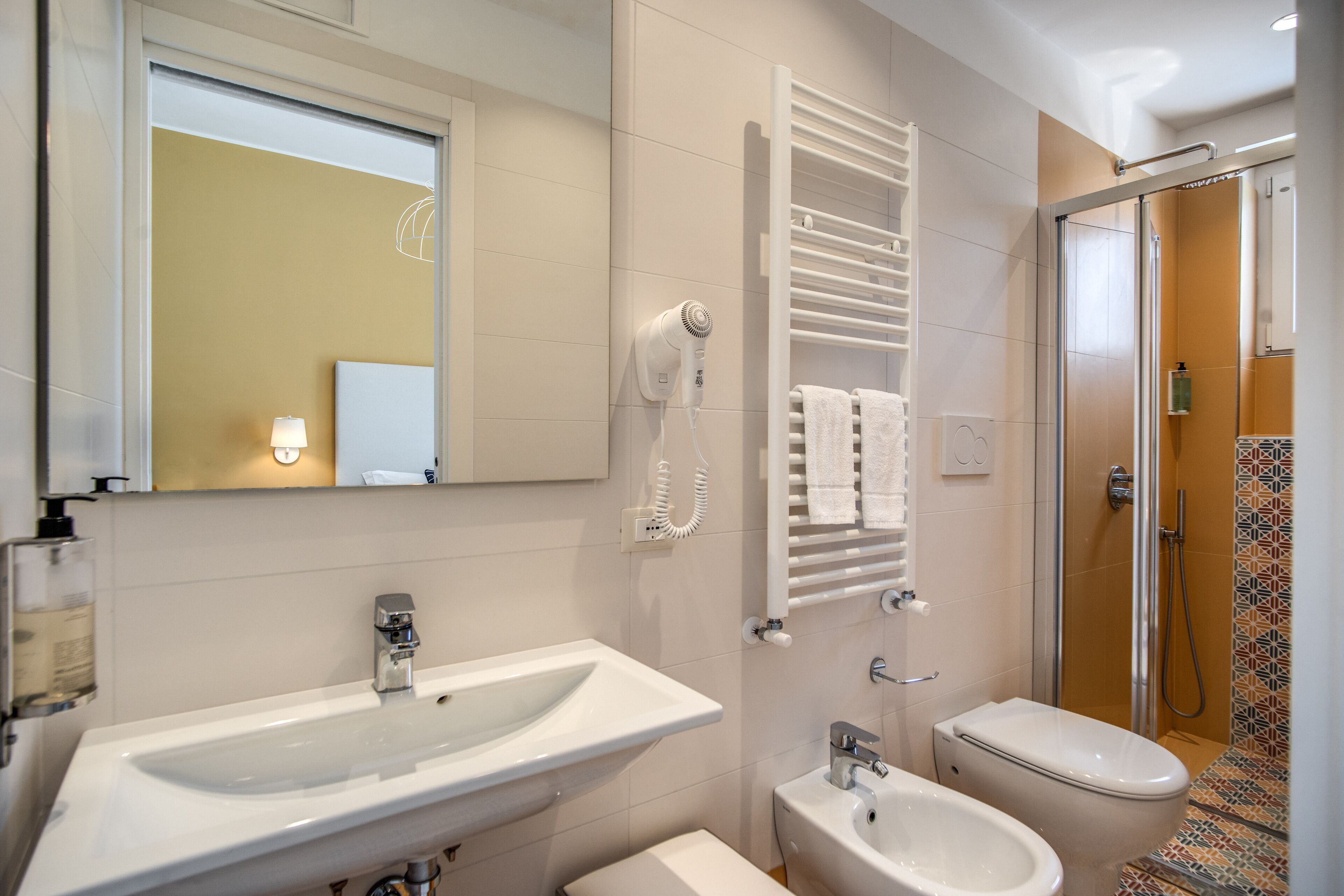 A modern bathroom with a large sink, a bidet, a toilet, a hairdryer mounted on the wall, and a shower area.