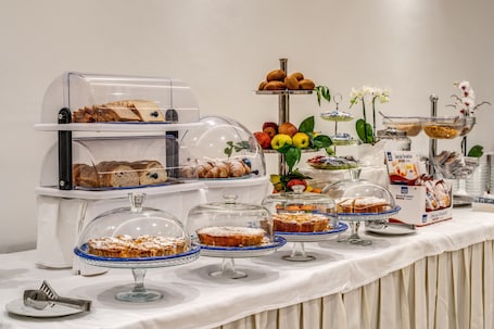 A buffet with various baked goods, fruits, and a coffee station.