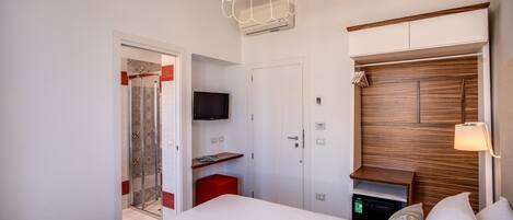 A modern hotel room with a large bed, a TV mounted on the wall, a wooden headboard, and a red accent wall.