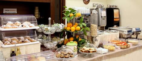 A buffet with various food items, including pastries, bread, and fruits.