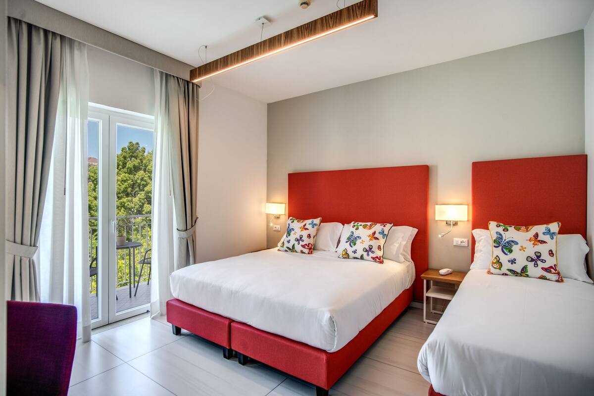 A hotel room with two beds, a balcony, and a view of trees.