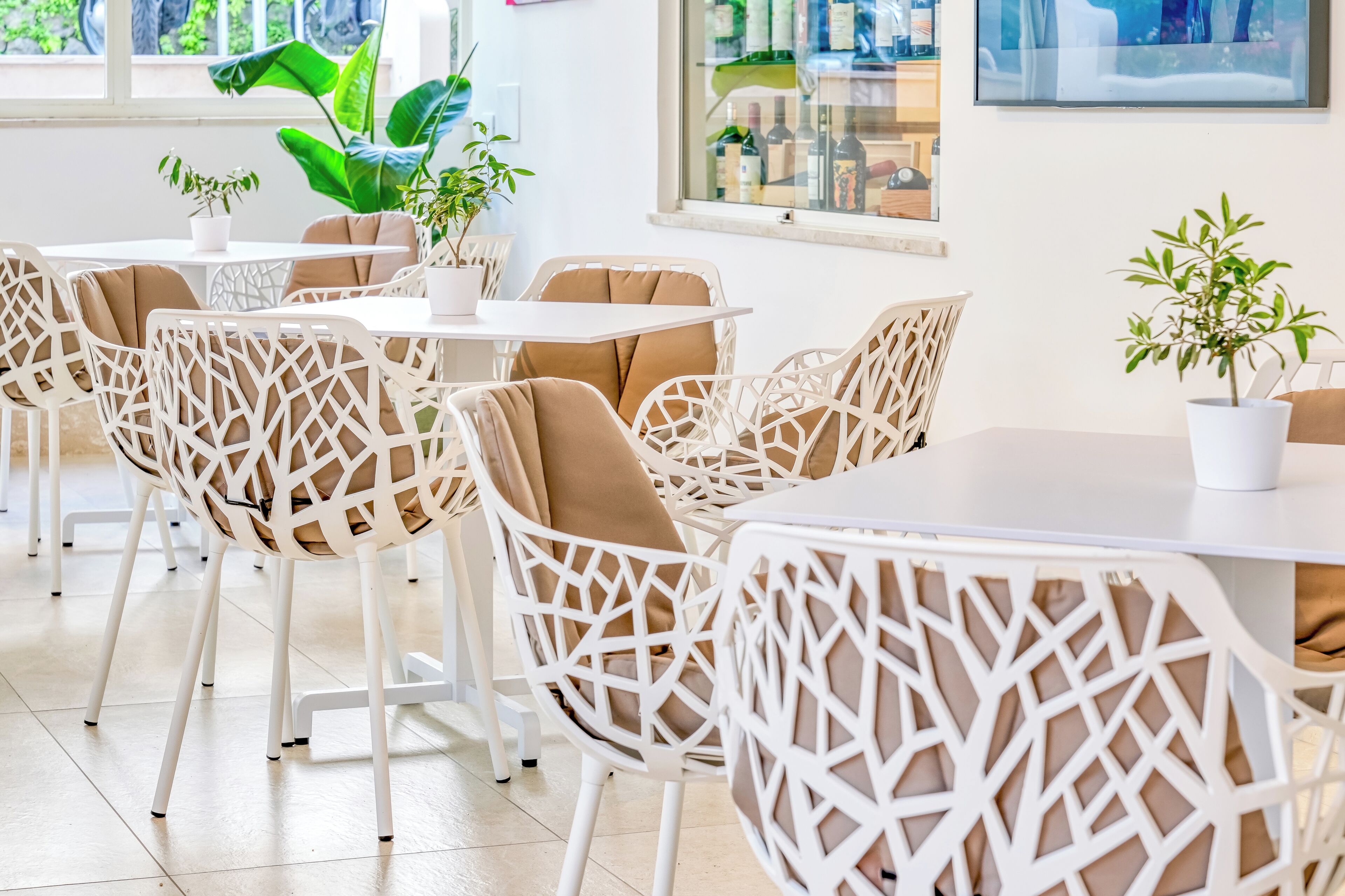 Un comedor moderno con sillas de mimbre blanco, cojines color beige y plantas en macetas.