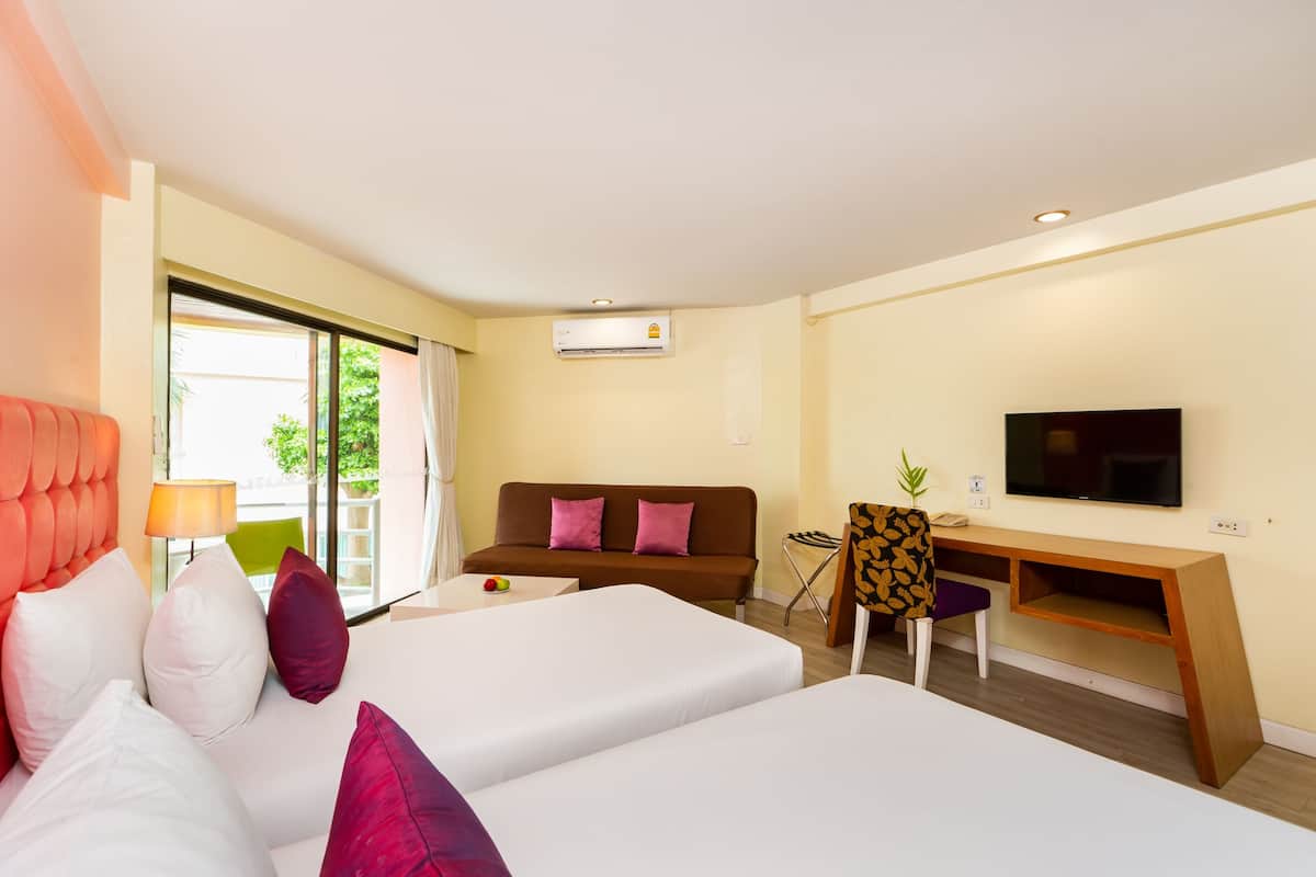 A hotel room with two beds, a sofa, a desk, a TV, and a window with a view of greenery.