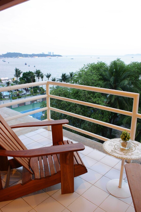 A balcony with a wooden chair and a small table, overlooking a pool and palm trees. - Bella Villa Metro (Pattaya)