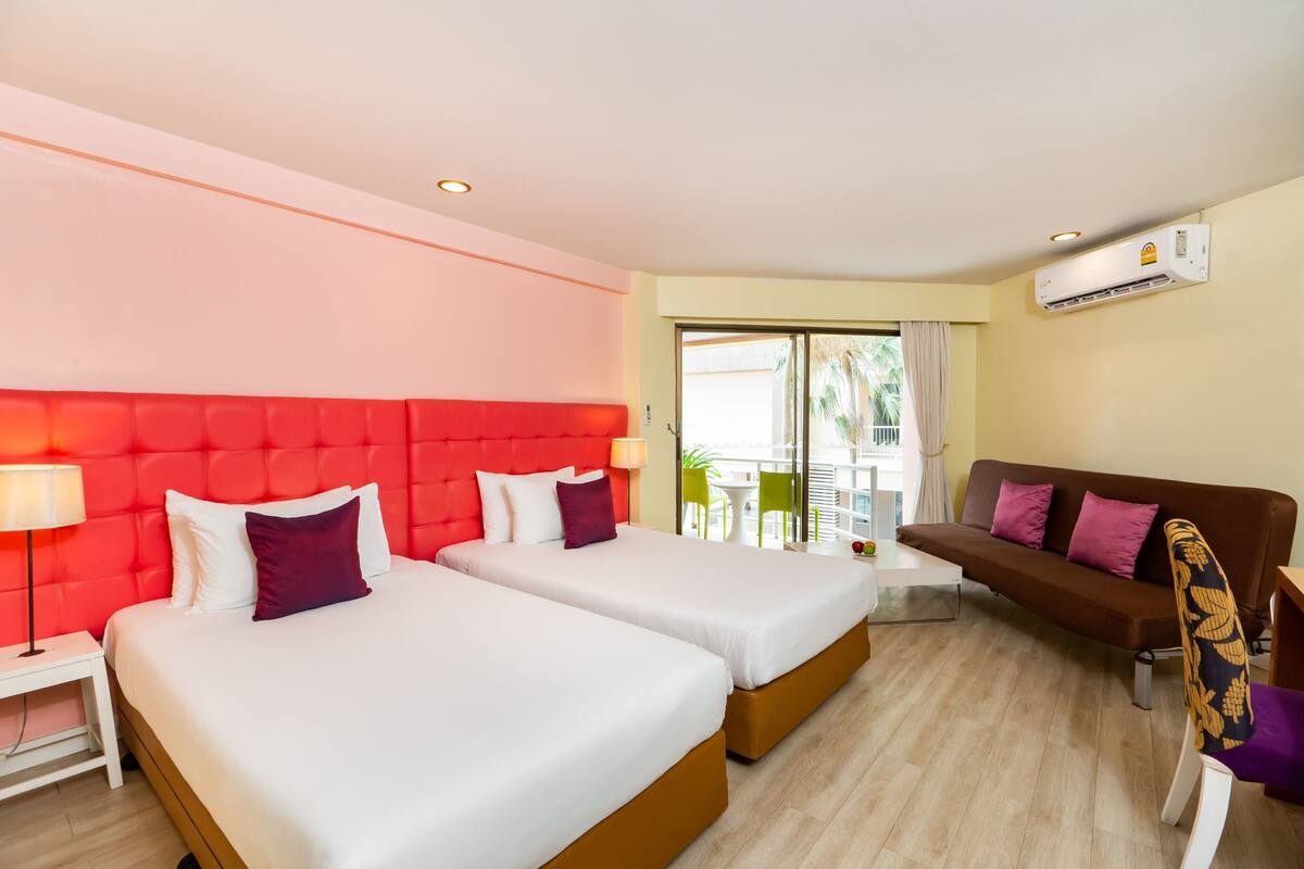A hotel room with two beds, a sofa, a dining table, and a balcony with a view.