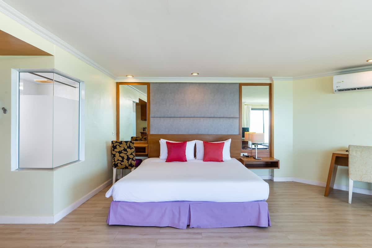 A hotel room with a large bed, a bedside table, a chair, a wardrobe, and a mirror.