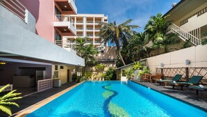 A swimming pool with lounge chairs and palm trees, surrounded by buildings with balconies and a staircase. - Bella Villa Metro (Pattaya)