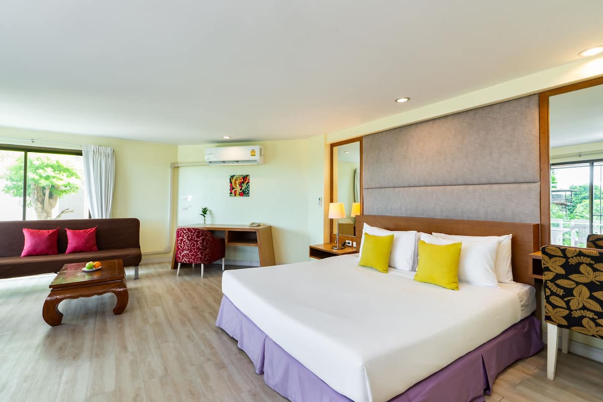A hotel room with a large bed, a desk, a sofa, and a chair.