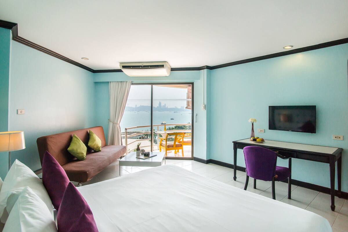 A hotel room with a bed, a desk, a chair, a TV, and a balcony with a city view.