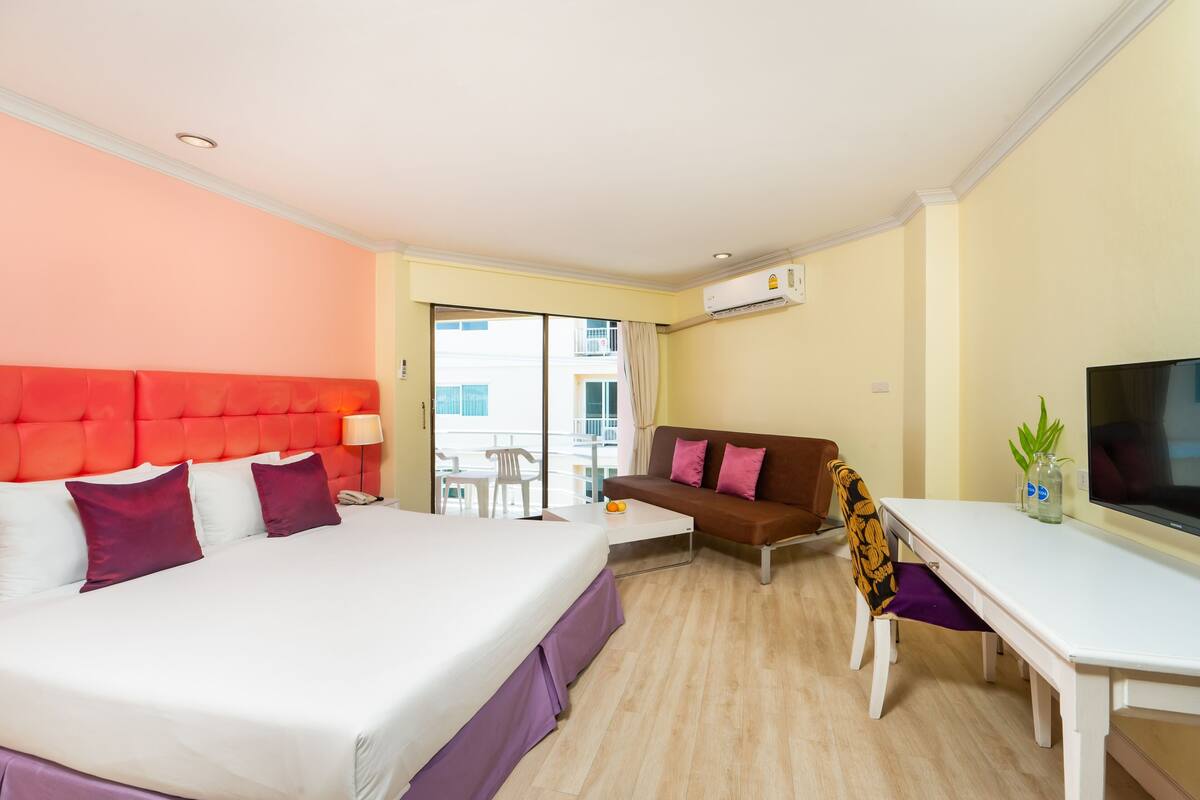 A hotel room with a bed, a sofa, a desk, and a TV.
