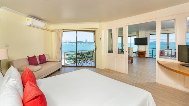 A hotel room with a large bed, a sofa, a TV, and a balcony with a view of the sea. - Bella Villa Metro (Pattaya)