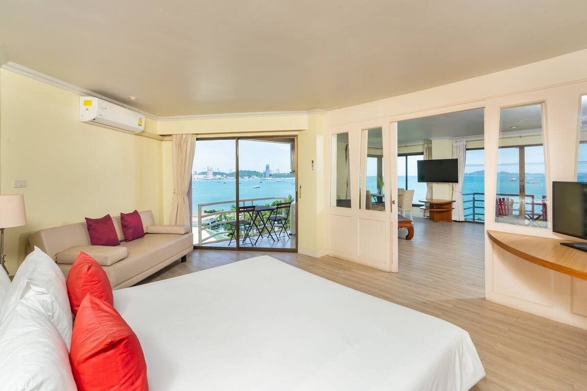 A hotel room with a large bed, a sofa, a TV, and a balcony with a view of the sea.