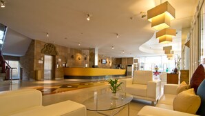Un moderno vestíbulo de hotel con una recepción, zona de estar y un amplio ventanal con vistas al interior.