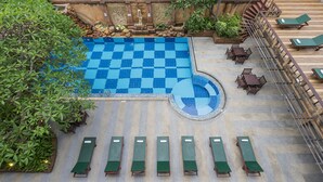 Una piscina en la azotea con baldosas a cuadros, rodeada de sillas de descanso y una escalera que lleva a un nivel superior.