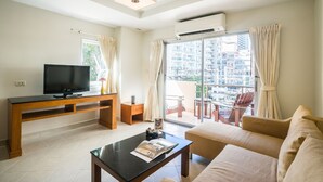 Una sala de estar moderna con un televisor de pantalla plana, una mesa de centro de madera, un sofá y un balcón con vistas a la ciudad.