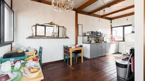 Una cocina amplia con vigas de madera, un candelabro y un comedor con una mesa lista para el desayuno.