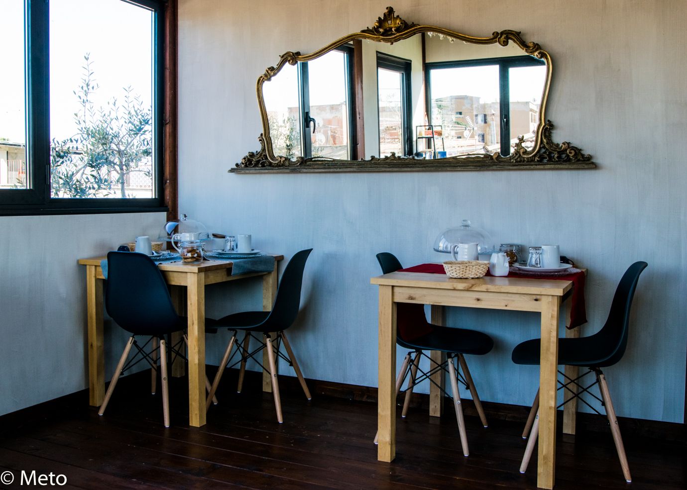 A room with two wooden desks and chairs, a large mirror, and a window with a view of buildings.