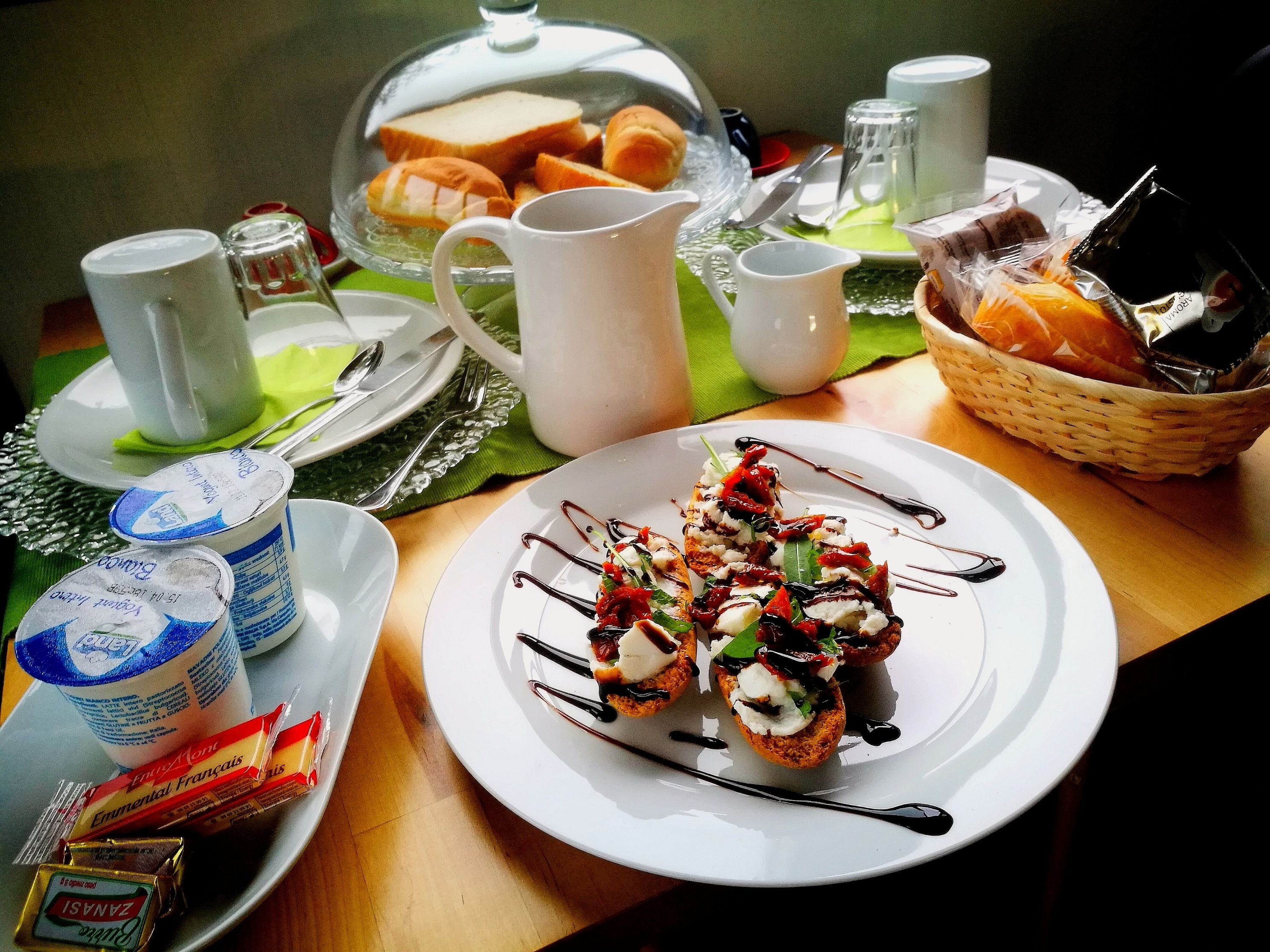 A breakfast setting with a plate of food, a basket of bread, and various condiments.
