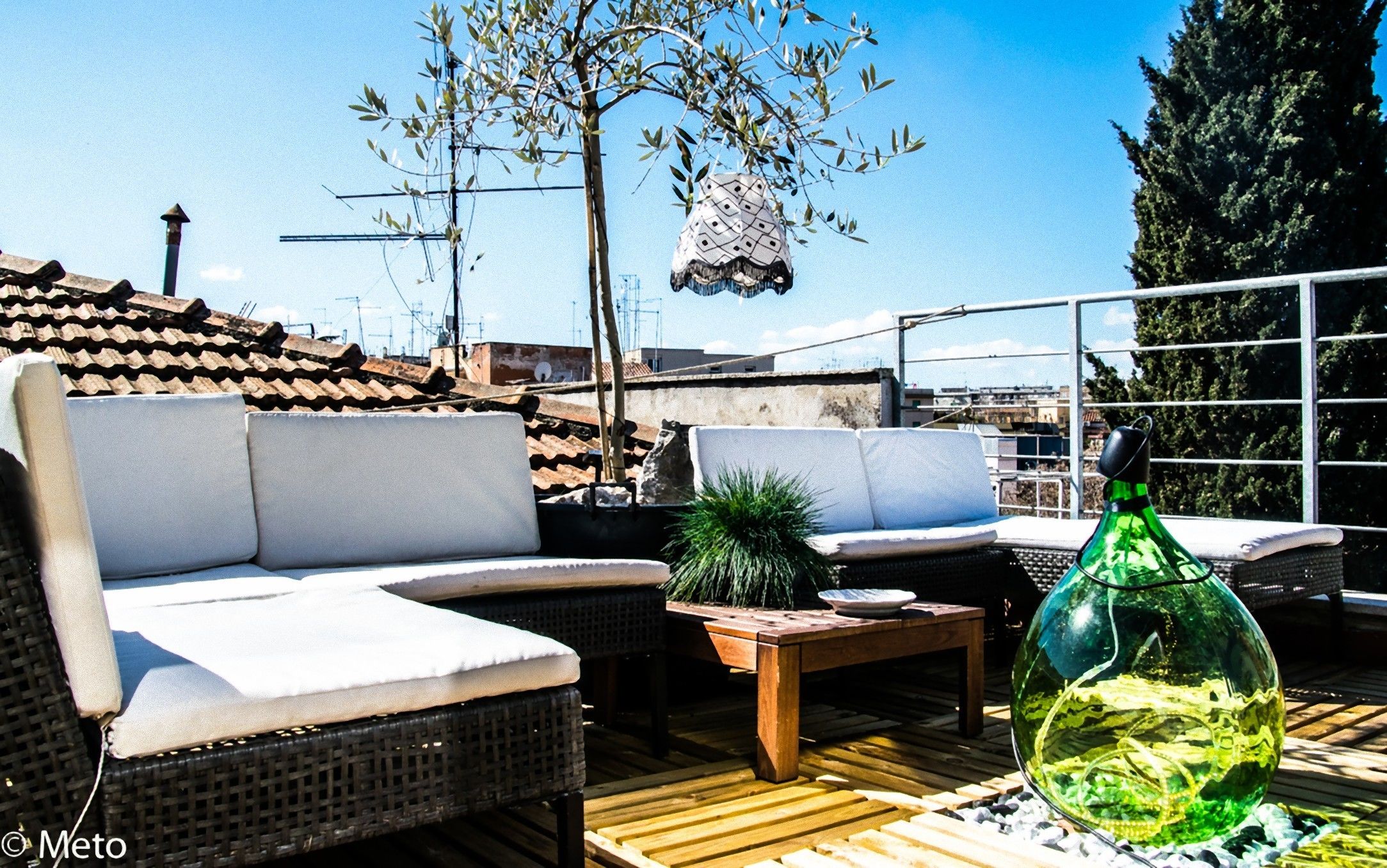 A rooftop patio with wicker furniture, a wooden table, and a decorative glass bowl.