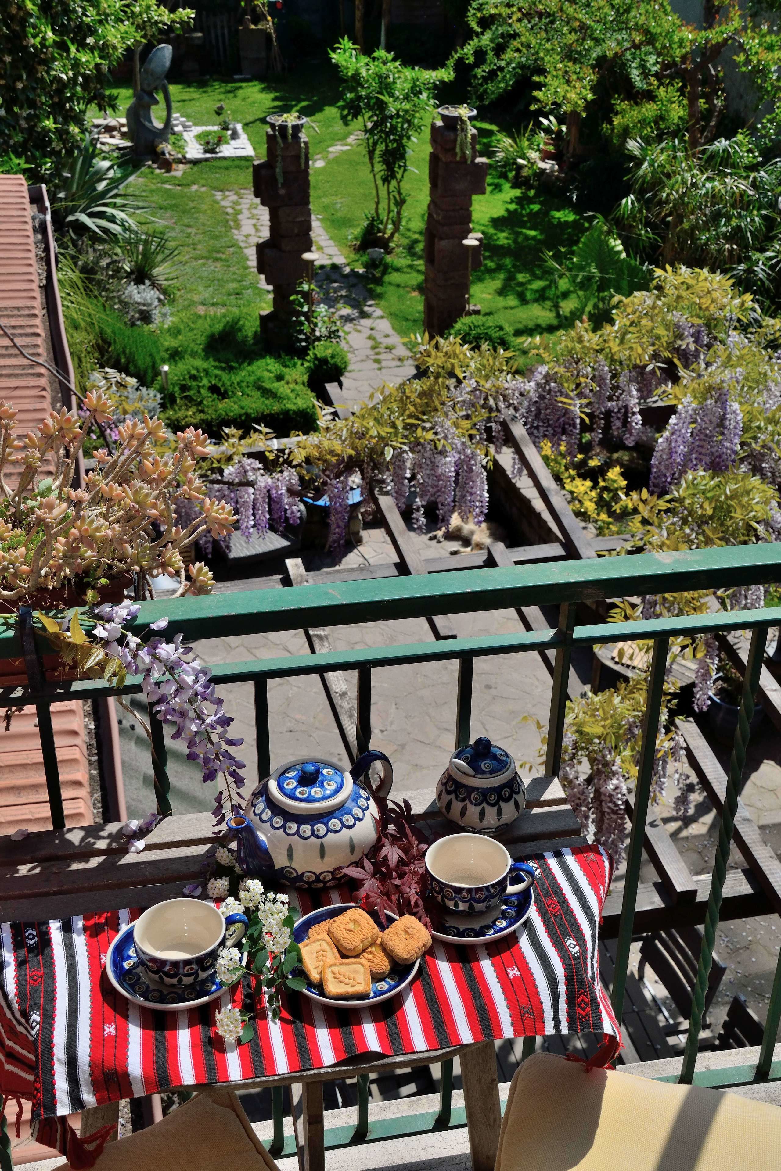 A balcony with a table set for tea, surrounded by lush garden views.