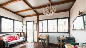 Una habitación acogedora con suelo de madera, un sofá con cojines rojos, una mesa de comedor con sillas y una araña.