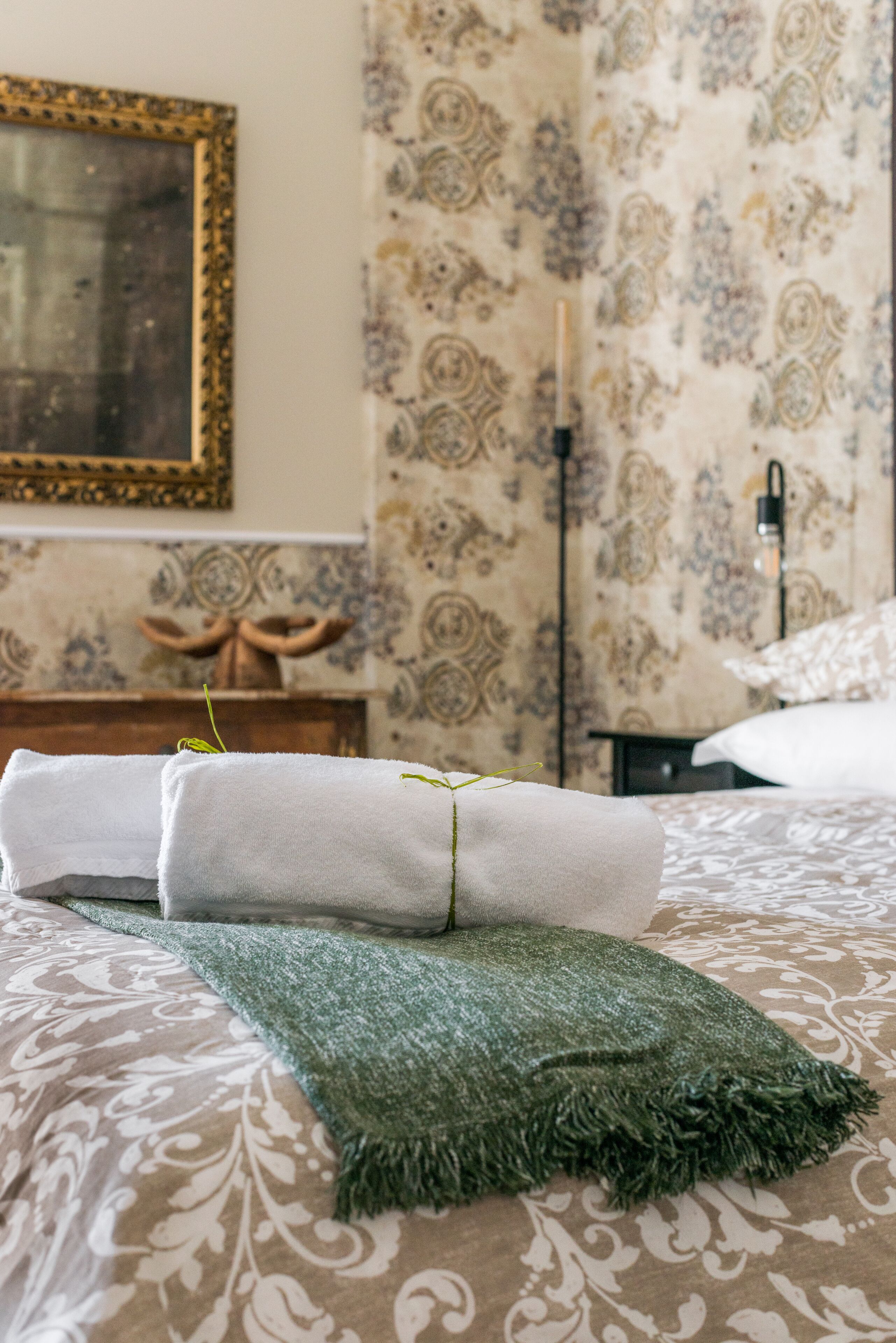 A neatly made bed with a green throw blanket and rolled towels.