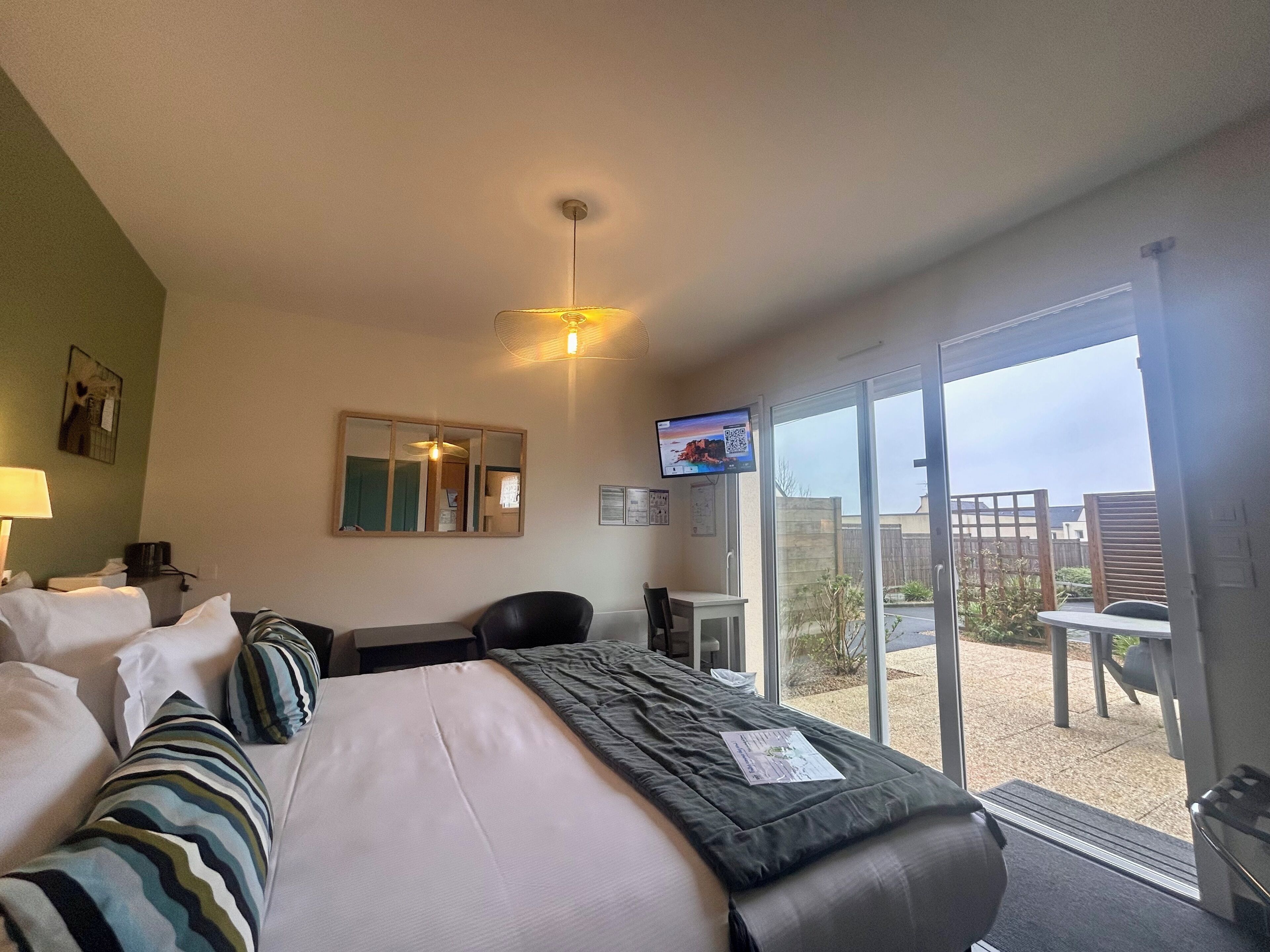 Una habitación de hotel con cama, escritorio, silla, televisión y balcón con vistas.