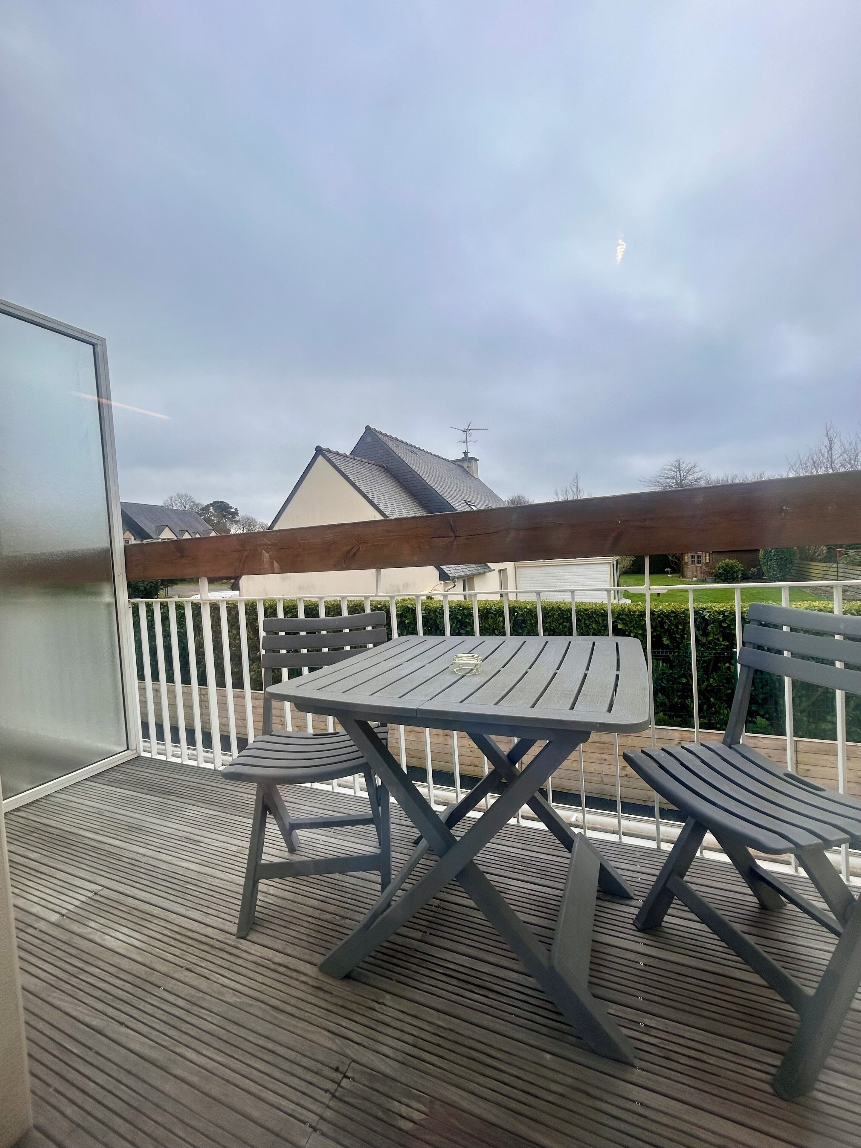 Un espace extérieur aménagé, abrité et doté d’une table et de chaises, d’une terrasse en bois et d’où l’on peut apercevoir une maison au loin.