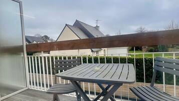 A covered outdoor seating area with a table and chairs, a wooden deck, and a view of a house in the background.
