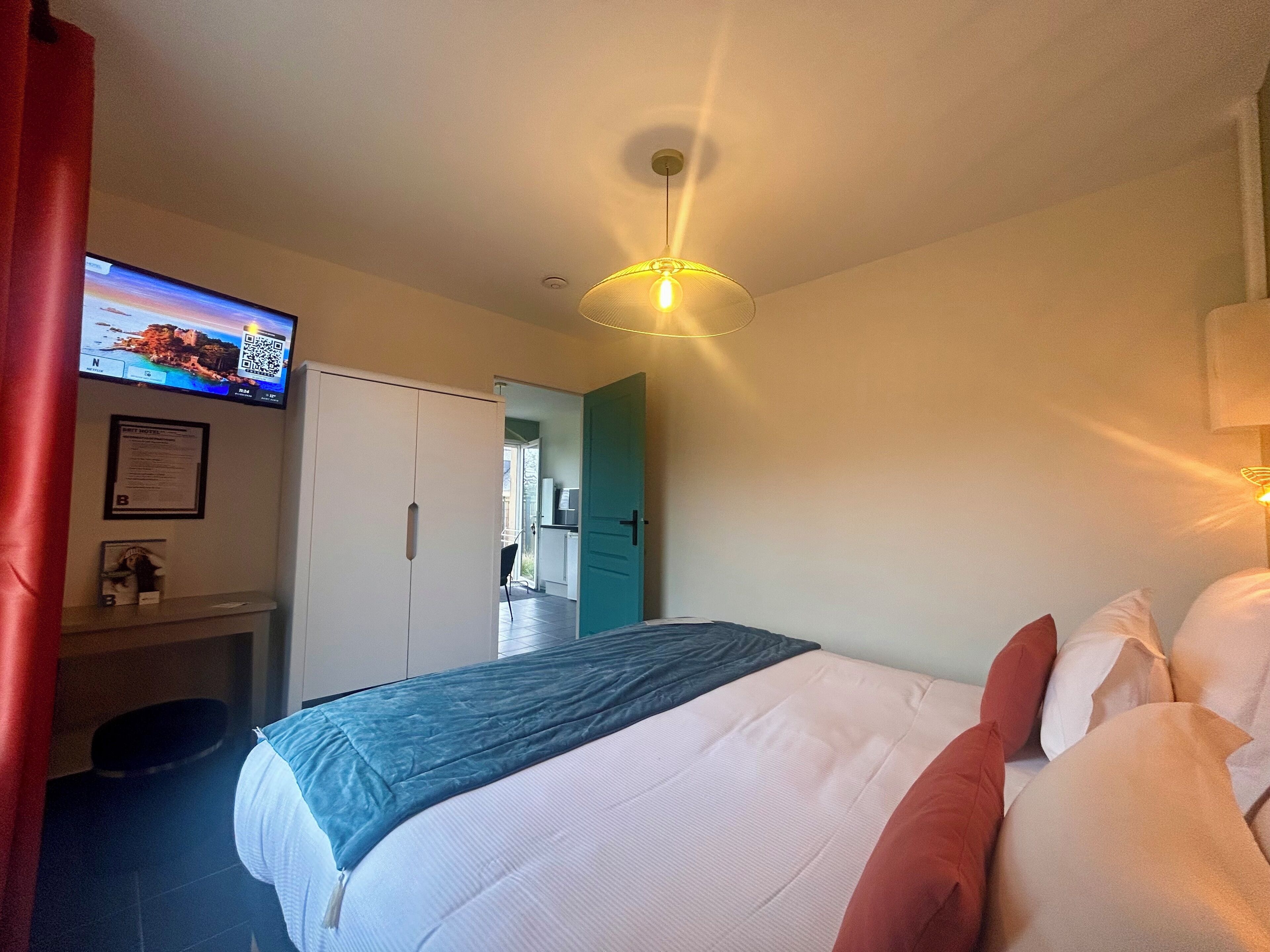 A hotel room with a bed, a desk, a television, and a door leading to a balcony.