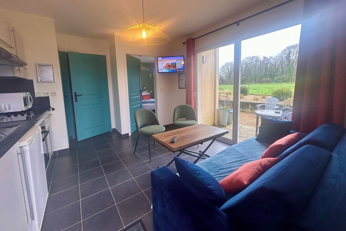 Een moderne kamer met een bank, een tafel en een televisie. Er is een kitchenette met een magnetron en een koelkast. De kamer heeft een groot raam en een deur die leidt naar een andere kamer.