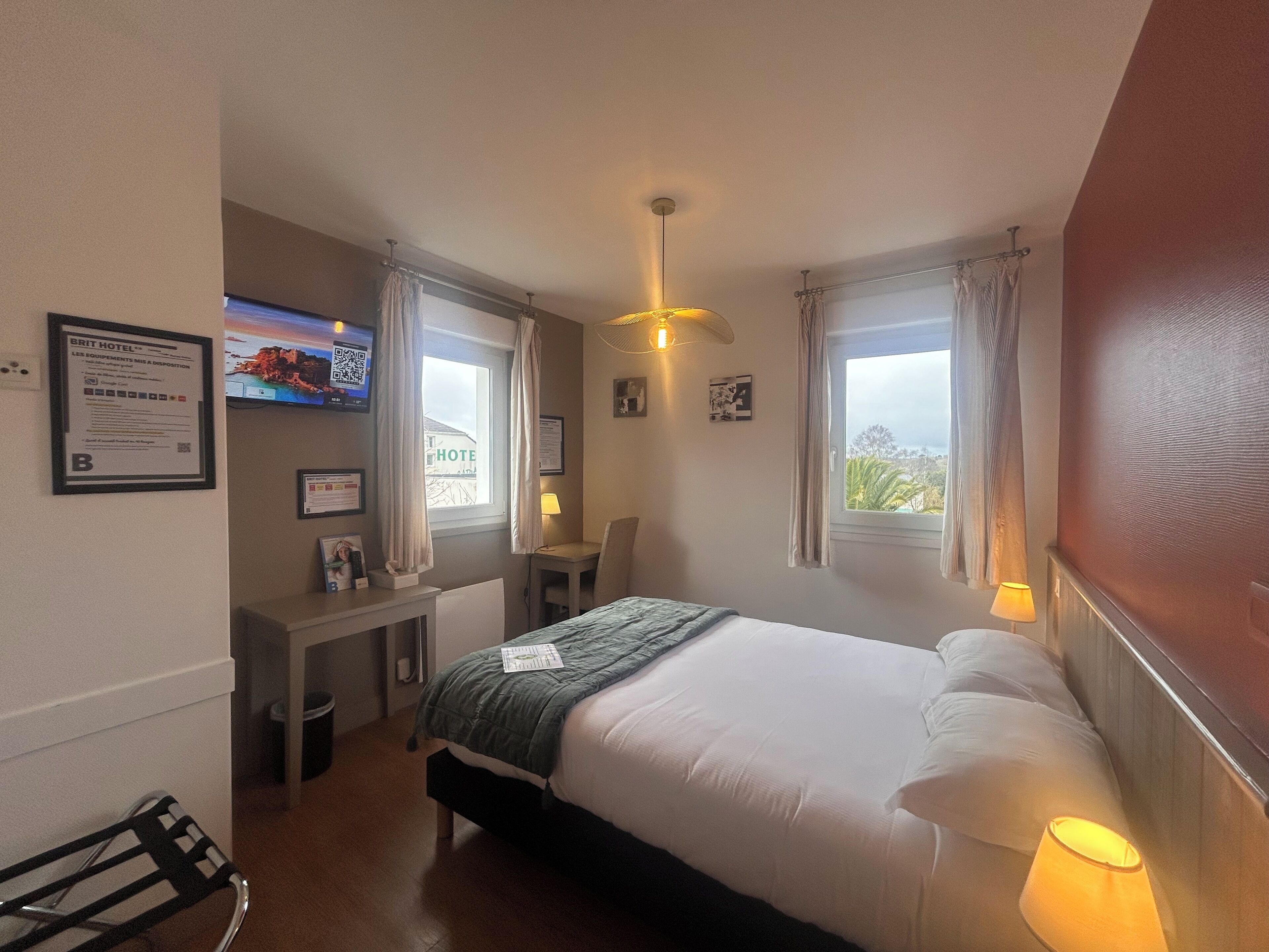 A hotel room with a bed, desk, chair, and a TV on the wall.