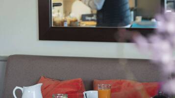 A breakfast table with a pitcher, bowl, and teapot, and a mirror reflecting a person in the background.
