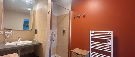 A bathroom with a glass shower enclosure, a sink with a hairdryer, a towel rack, and a small wicker basket.