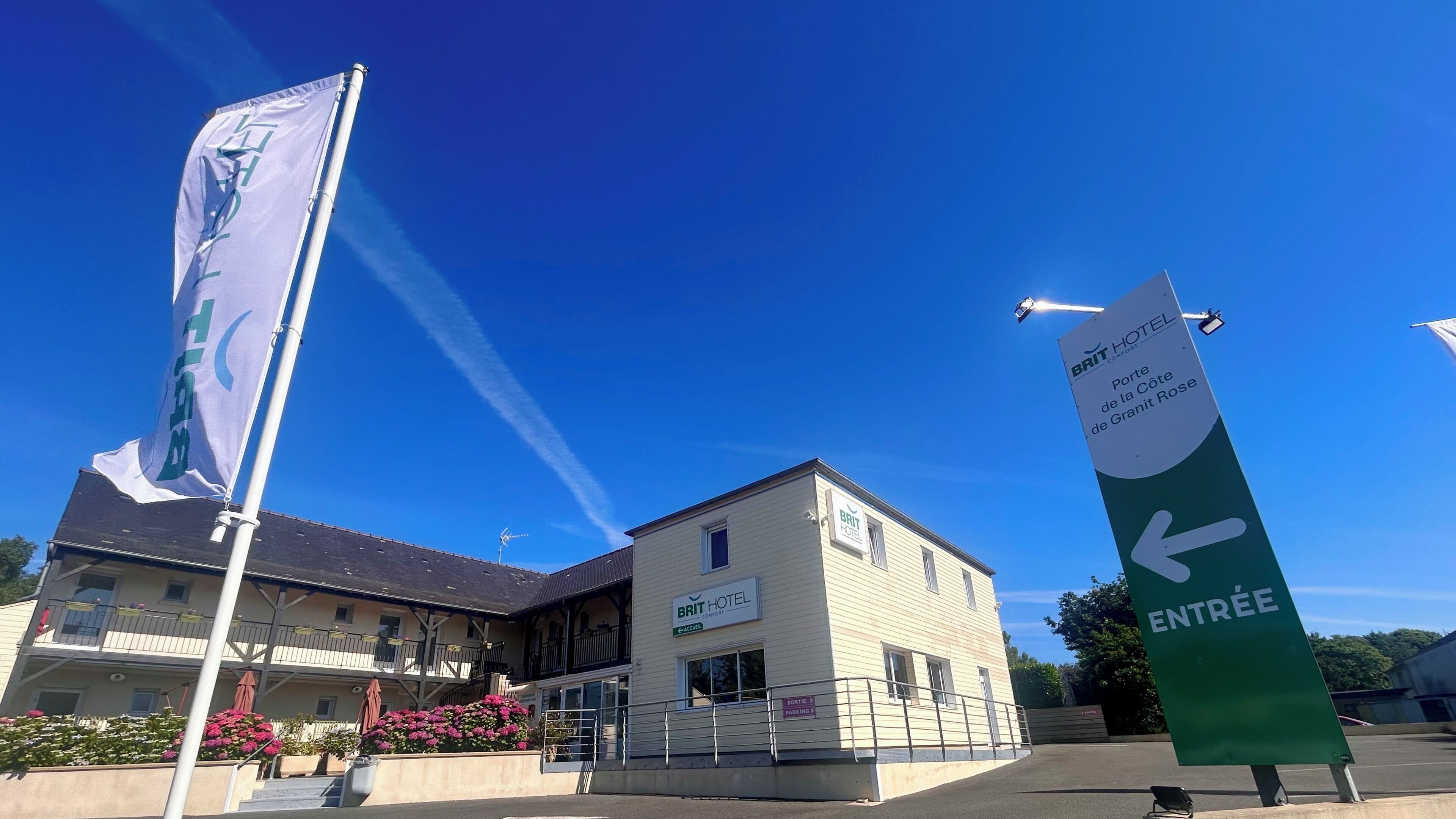 Un hotel con un cartello che indica l'ingresso, un asta con una bandiera e un edificio con balconi.