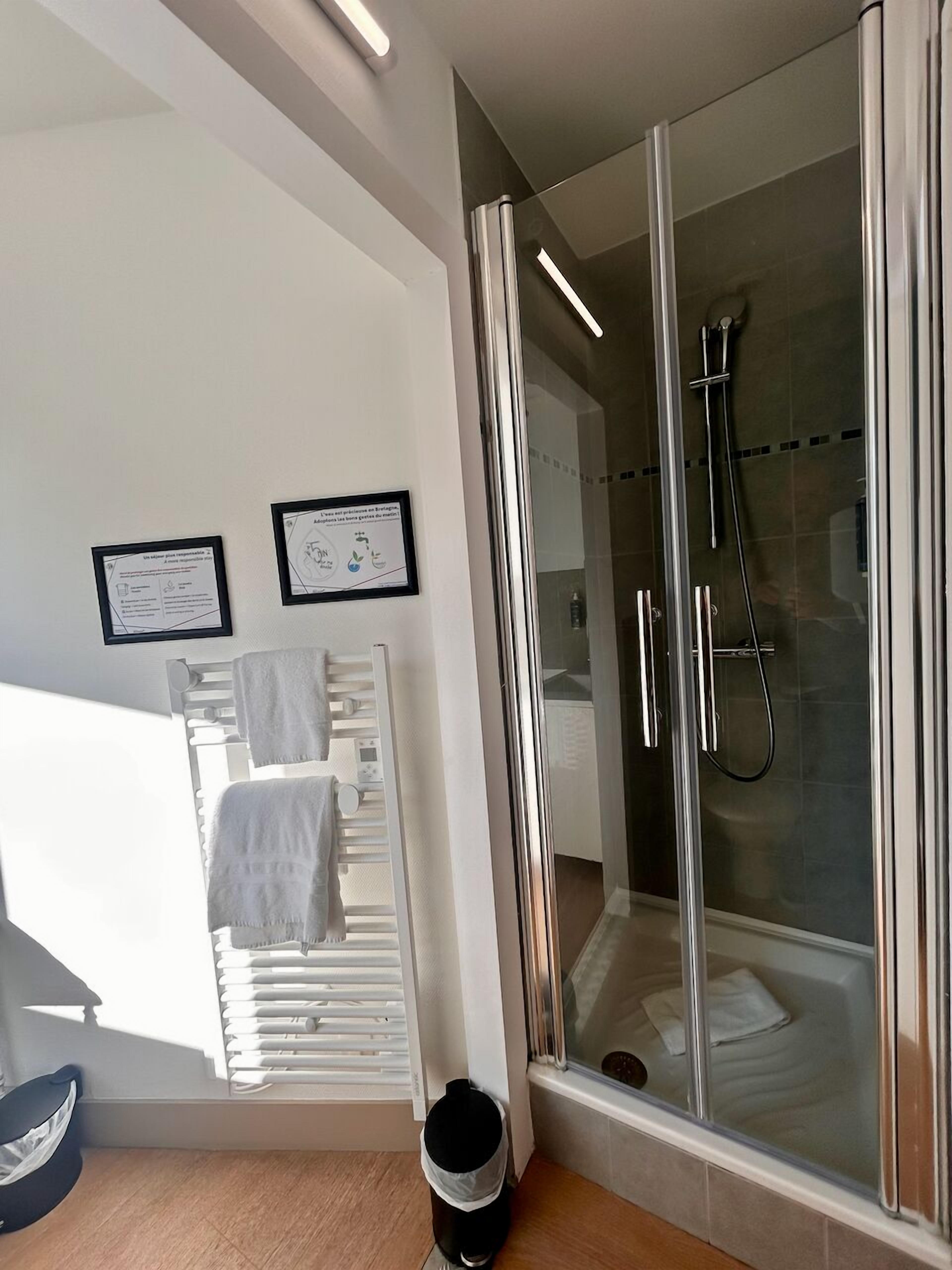 Un baño moderno con ducha acristalada, un perchero y dos carteles informativos en la pared.