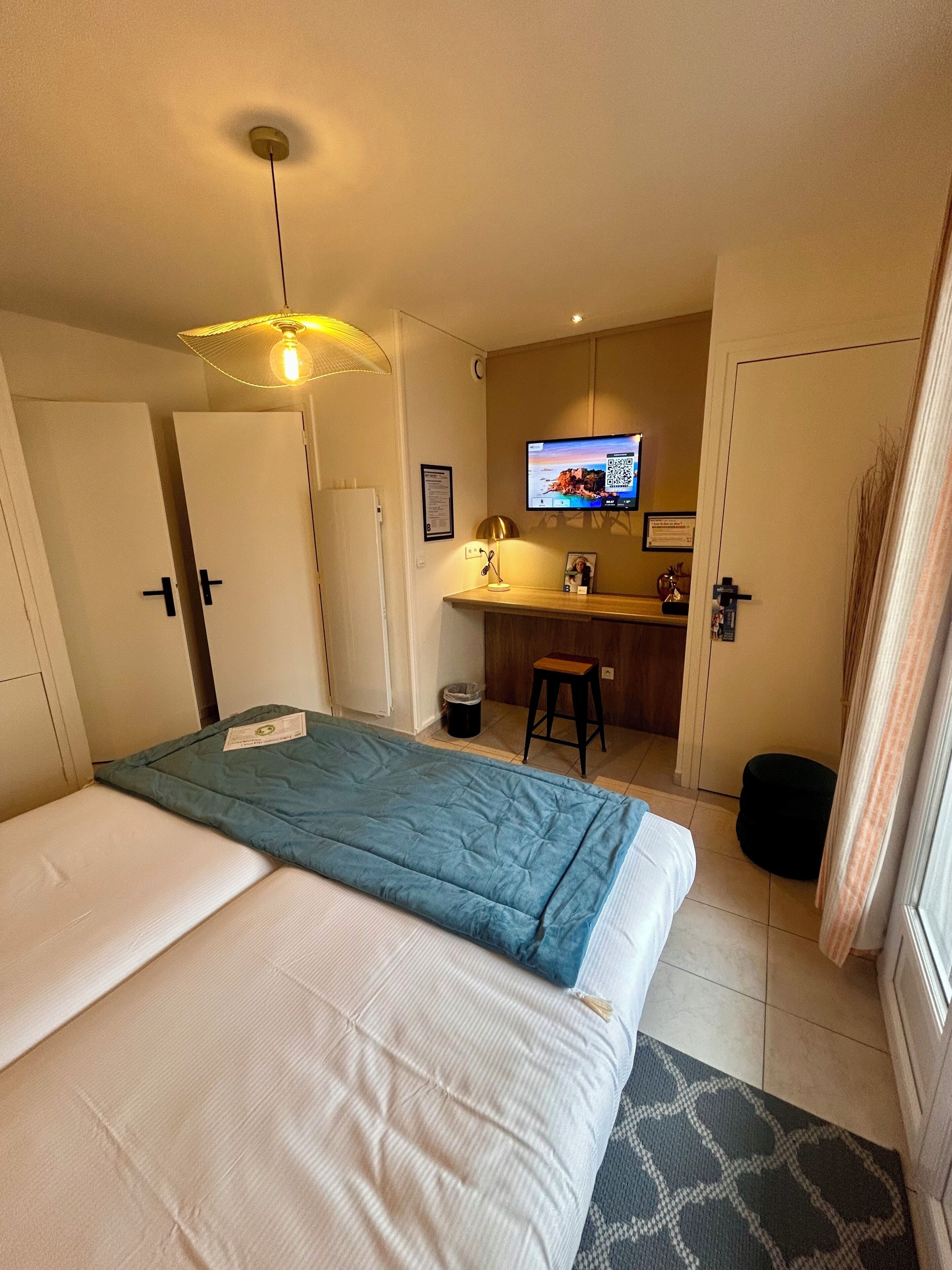 A hotel room with a bed, a desk, a television, and a small stool.