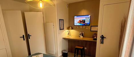 A hotel room with a bed, a desk, a television, and a small stool.