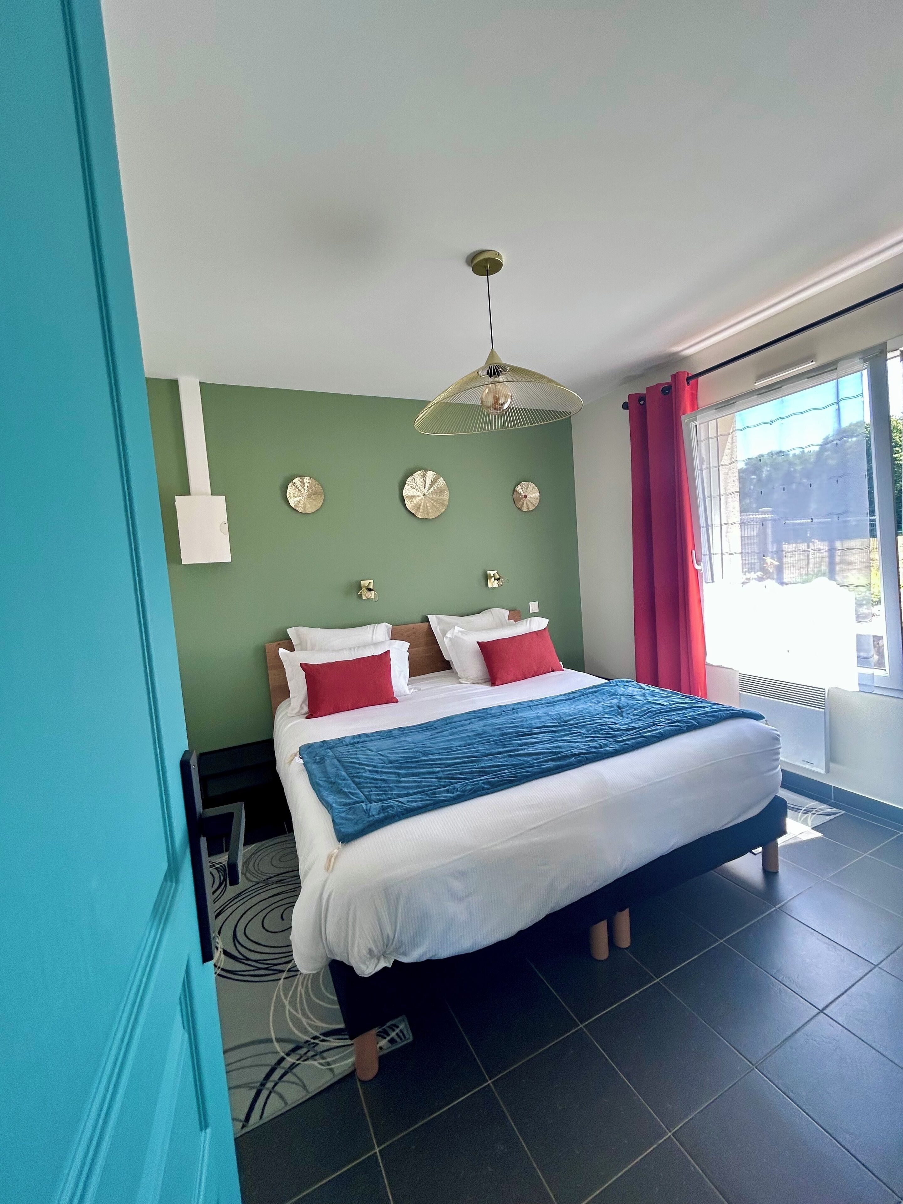 A bedroom with a bed, a hanging light fixture, a window with curtains, and a wall with decorative plates.